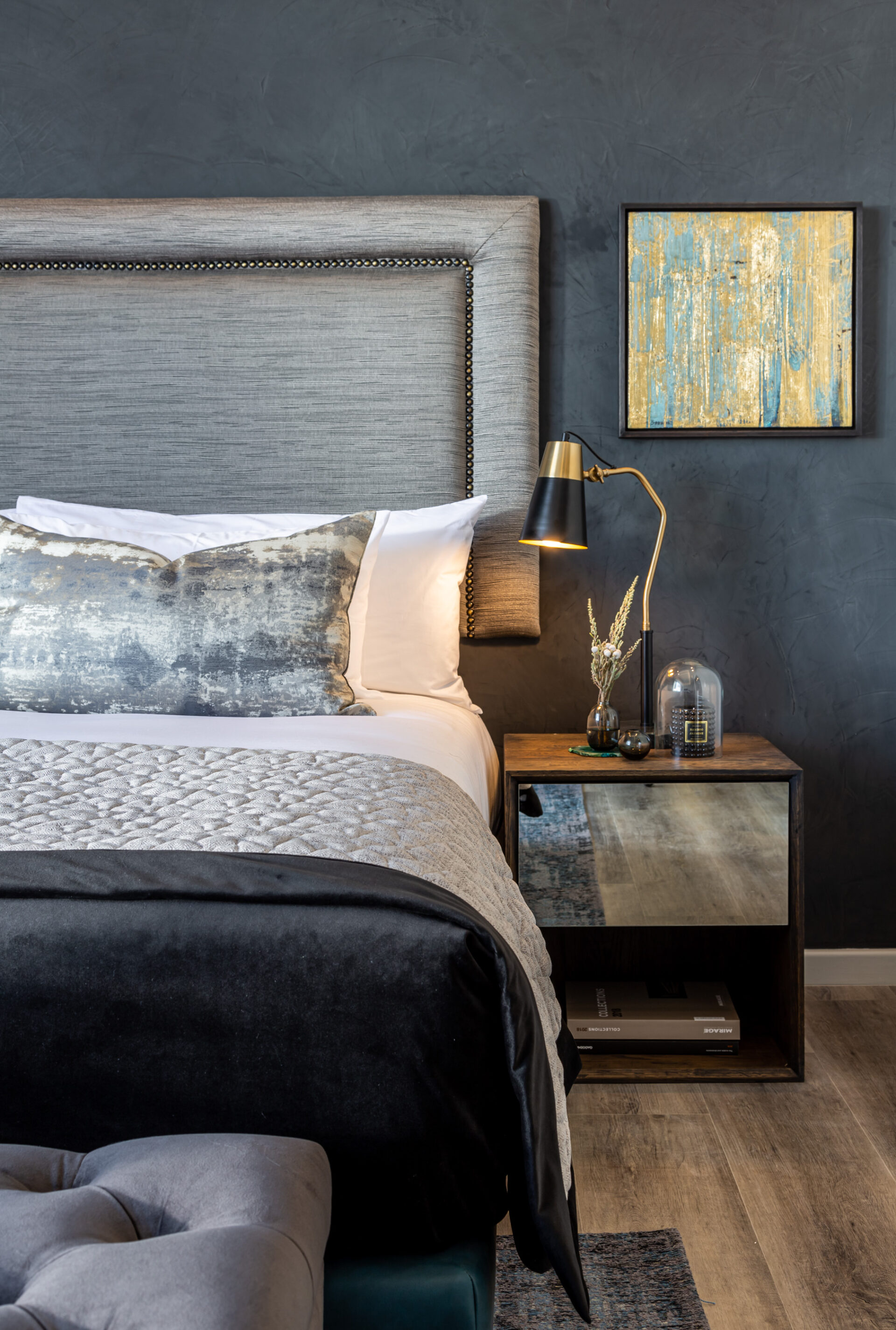 A luxurious double bed taking up the left hand side of the frame with a bedside table and lamp next to it