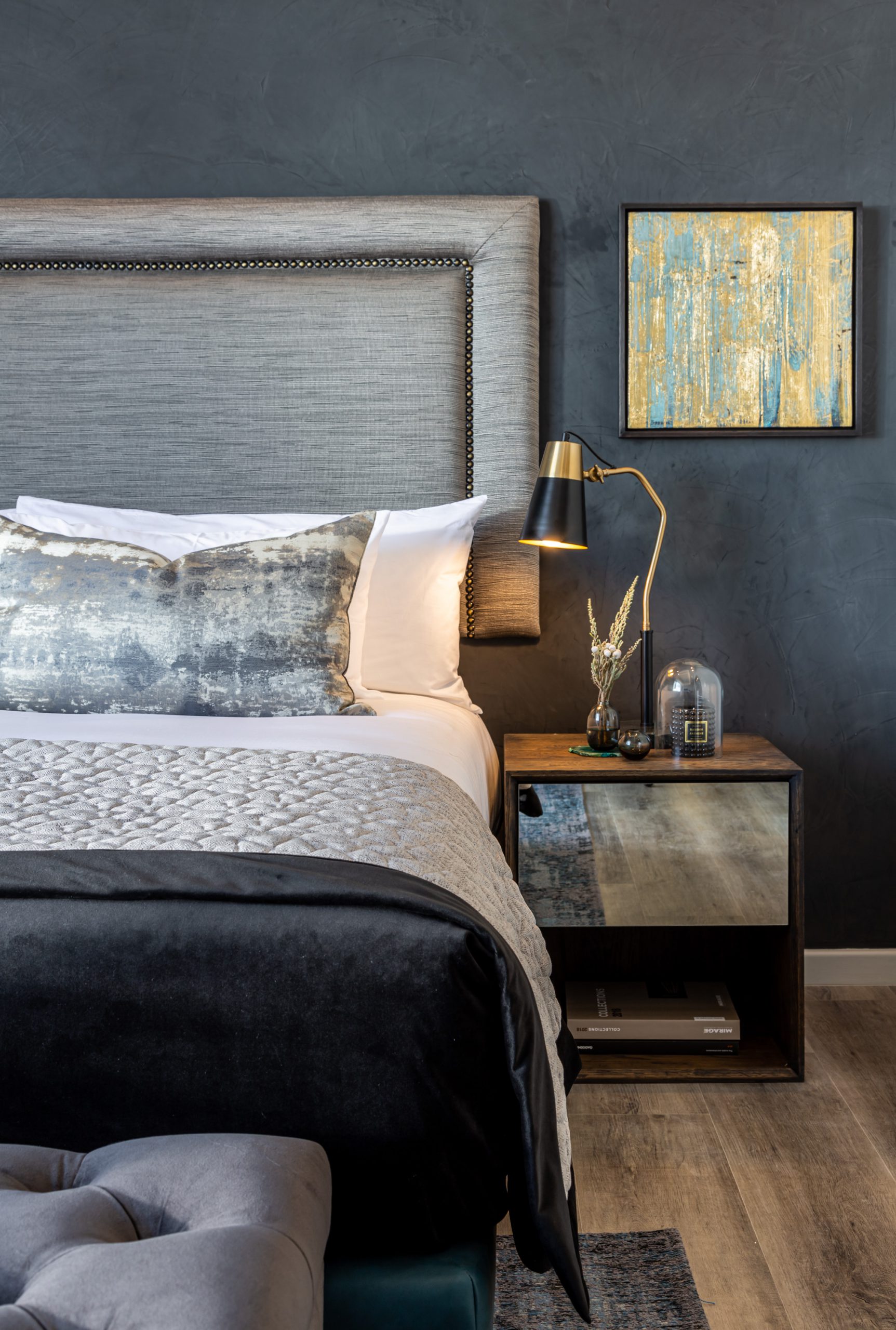 A luxurious double bed taking up the left hand side of the frame with a bedside table and lamp next to it