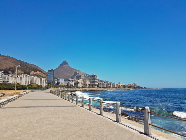 A promenade with buildings and Lions Head mountain behind it and the sea on the right hand side