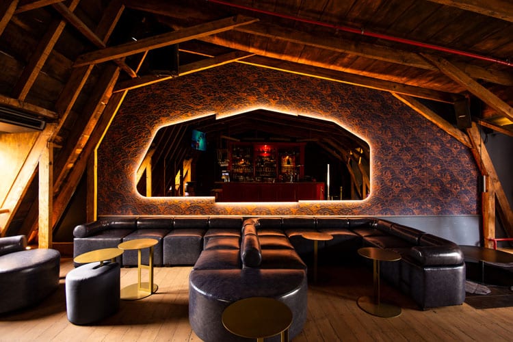 A room with wooden ceilings, dark leather seats, and a mirror on the back wall with architrave lighting