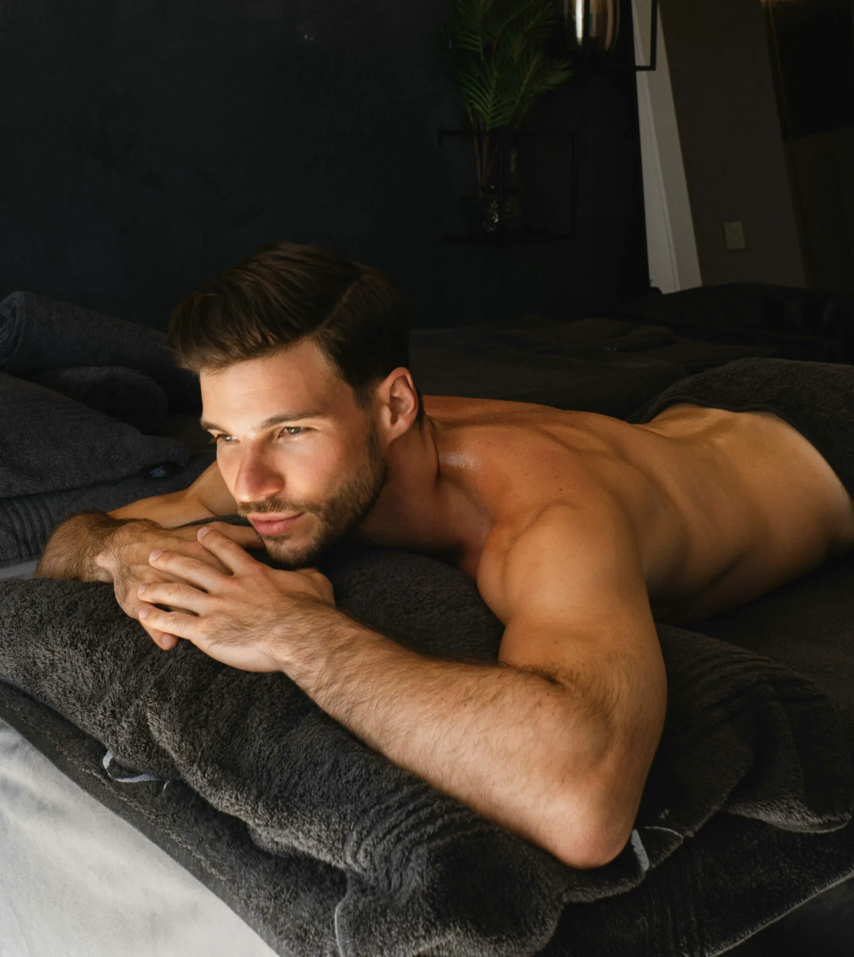 A shirtless male lying on a spa bed with charcoal grey coloured towels